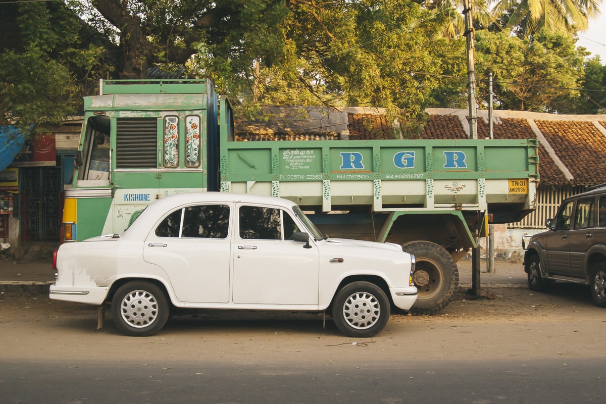 A white Hindustan Ambassador with a Green truck