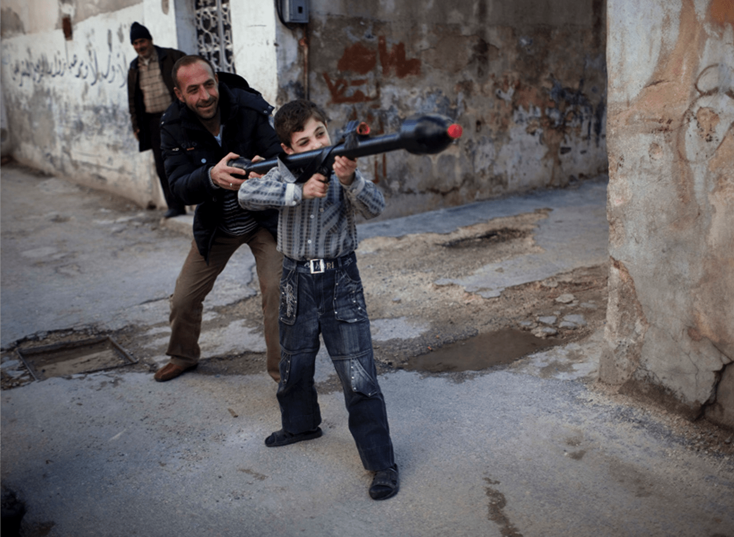 Pulitzer-Winning Photos: A man teaches Bilal, 11, how to use a toy rocket propelled grenade in Idlib, northern Syria, March 4, 2012. (Rodrigo Abd, Associated Press - March 4, 2012)