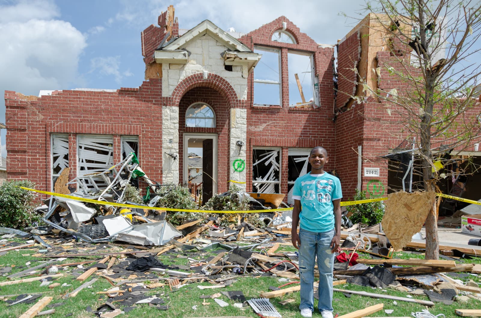 A kid standing in front of his home destroyed by a tornado