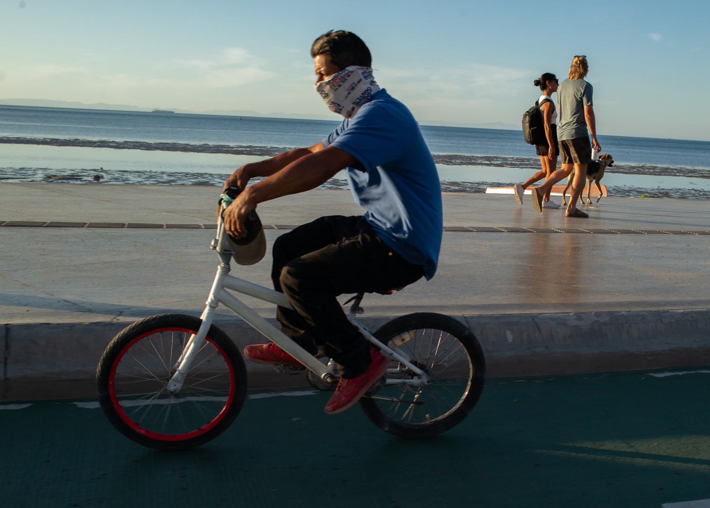 A man riding his bike with tourists walking in the background on the boardwalk in La Paz, Mexico