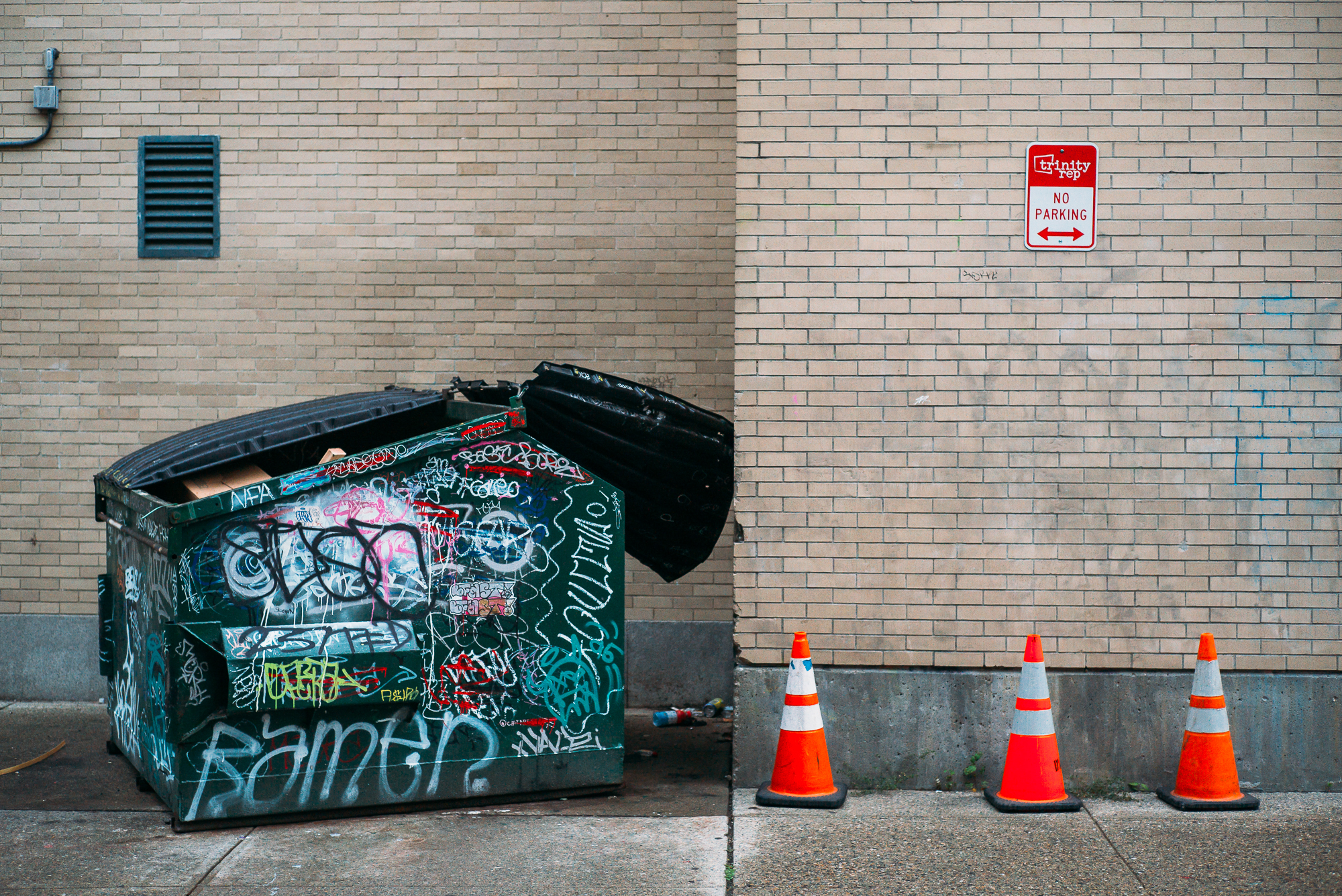A dumpster covered with graffiti and traffic cones in downtown Providence